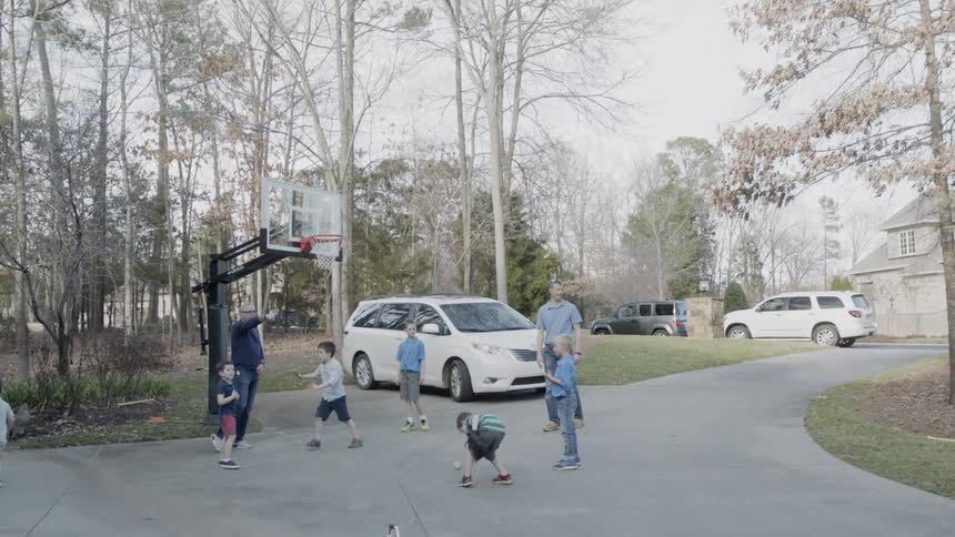 A group of boys and adults are playing in a driveway on a sunny day