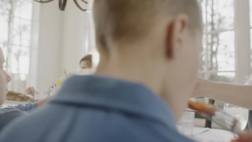 A family passes bowls of food to each other as they dine in a sunny room