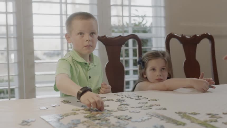 Two children sit at a table putting together a puzzle
