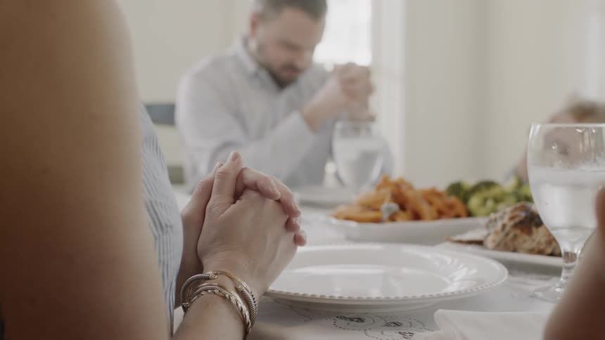 Man and woman clasp their hands in prayer as they sit at the dinner table