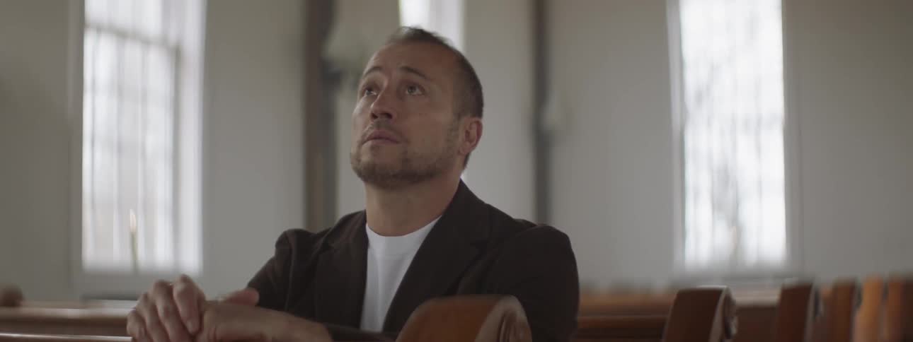 Man sits down in a church pew and bows his head
