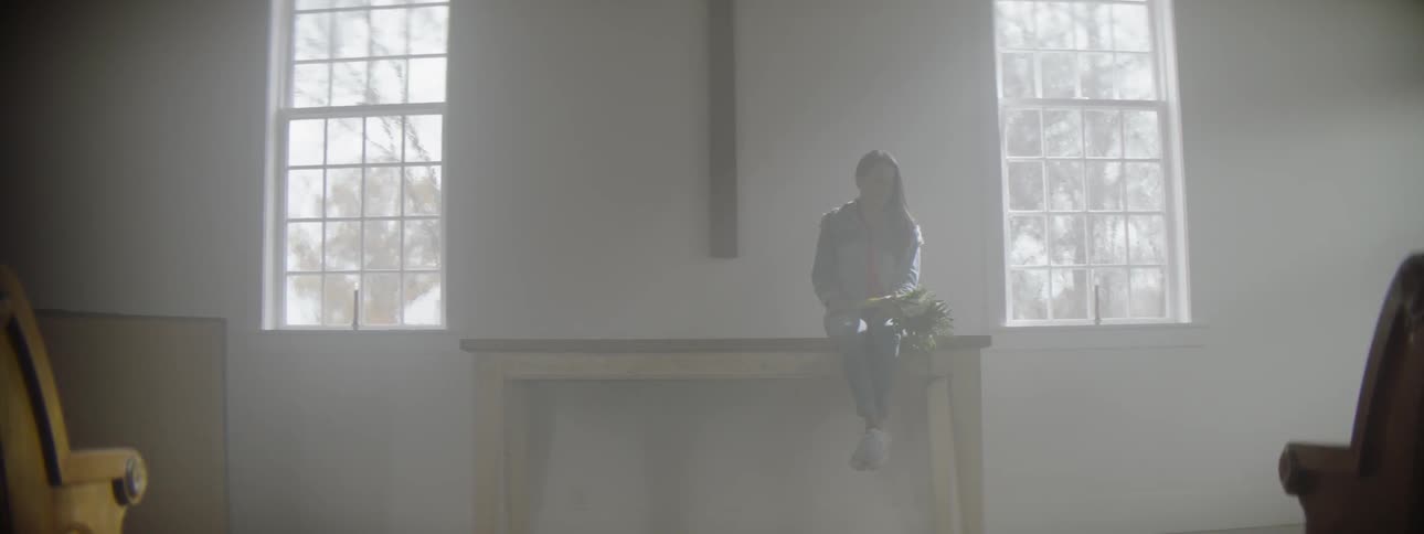 Person sits on a tall table under a cross near two windows