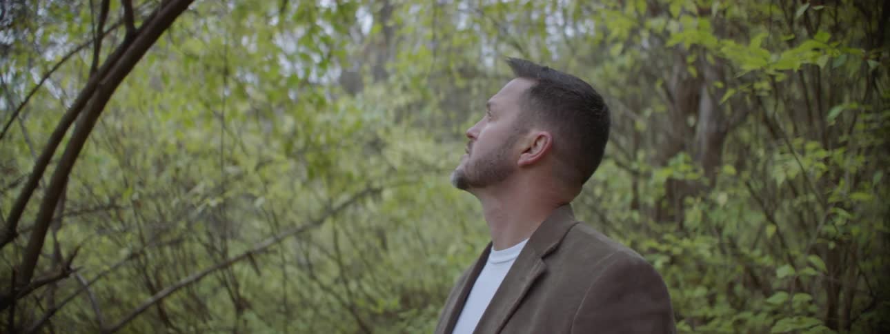 Man stands in the woods looking up through the trees
