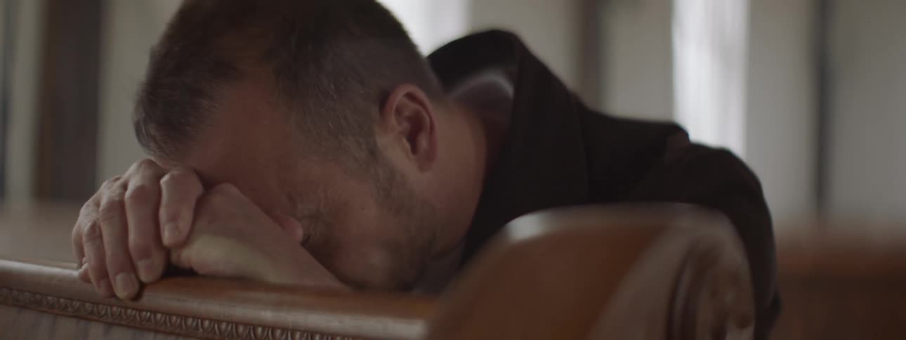 A man is leaning forward on the pew