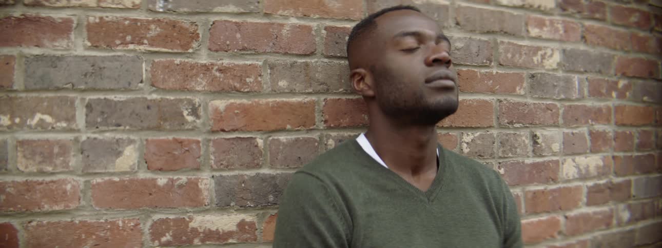 Man leans against a brick wall outside