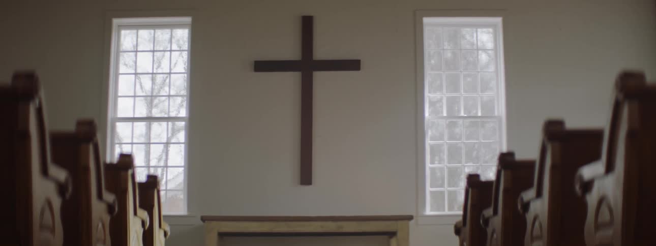 Cross on a wall near two windows and pews