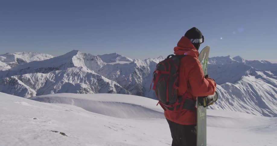 Man carrying snowboard uphill turns around to take in the view