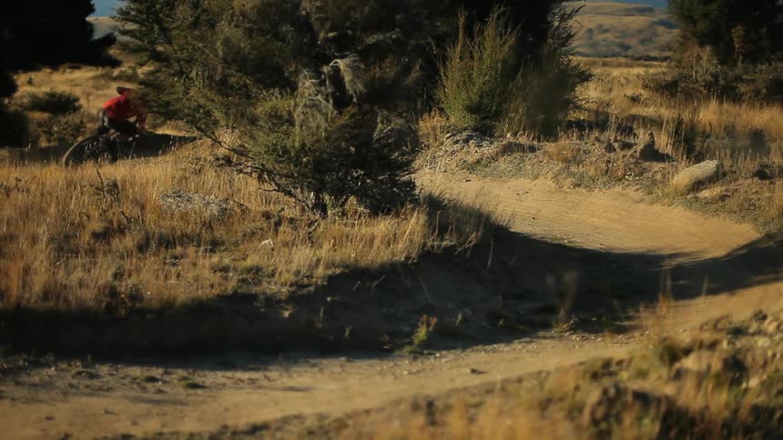 A man in a red shirt rides his bike down a dirt path