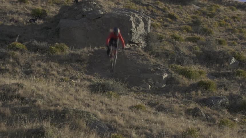 Man riding his bike down a steep hill jumps over a huge rock