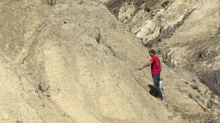 A man is spraying something on a dirt hill