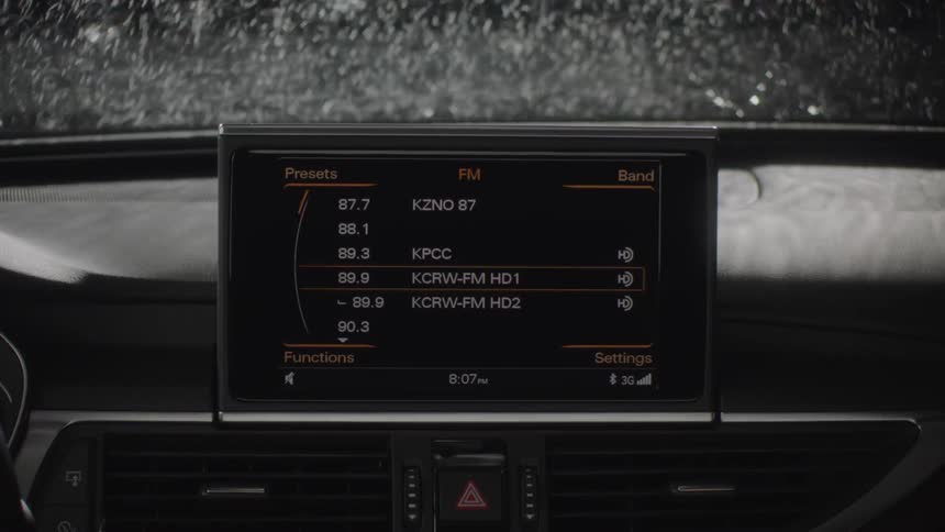 A screen on a car dashboard displays radio stations as it rains