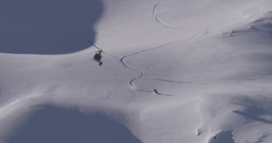A helicopter hovers over a snowboarder