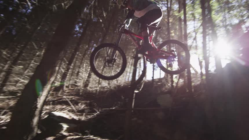 A person rides their dirt bike off a rocky ledge in the forest