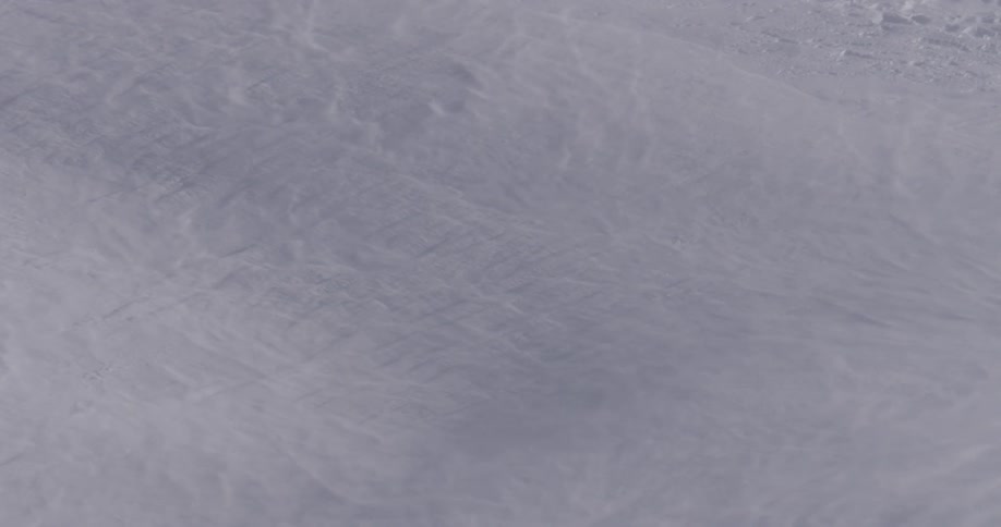 Wind slowly blows snow down a hill