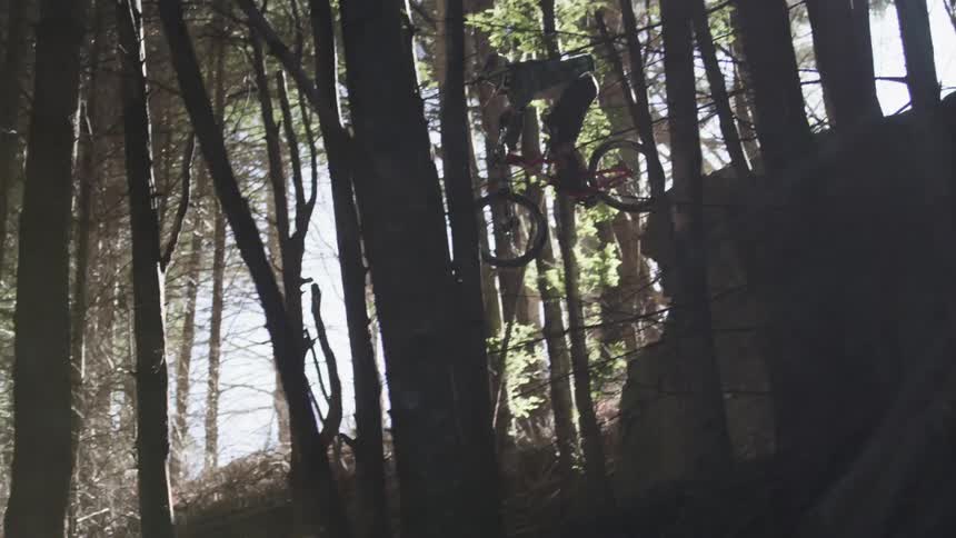Man riding his bike does a jump off a small cliff in the woods