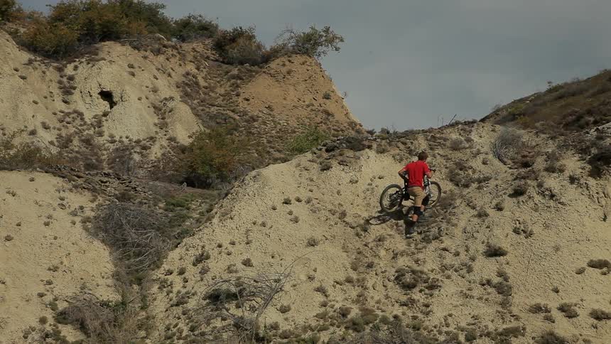 A young man carries his mountain bike up a steep and sandy hill