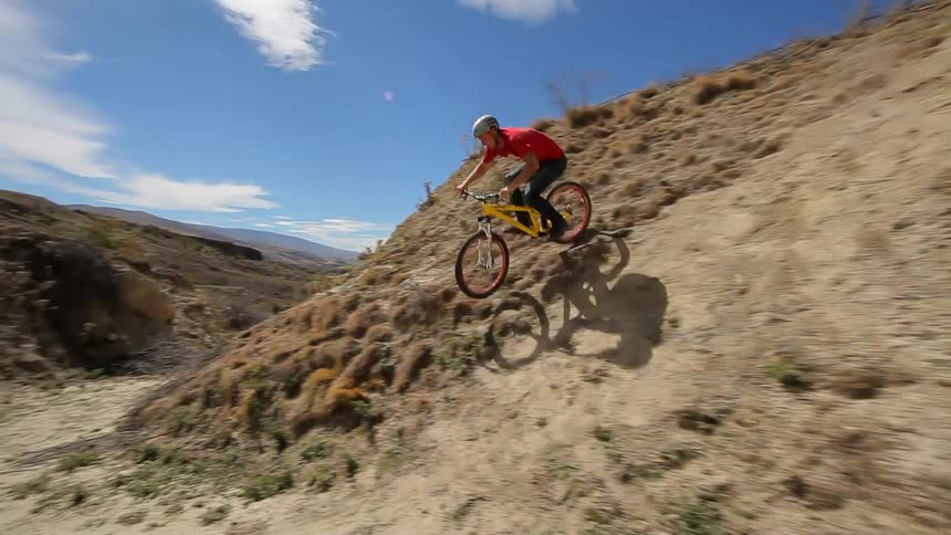 A man in a red shirt does bike tricks on a desert mountain