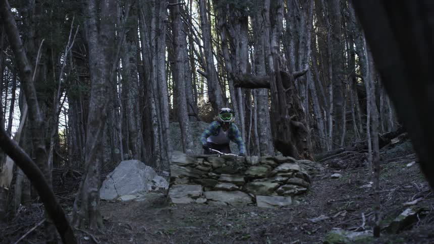 Someone riding their bike and jumping it off the edge on a forest trail