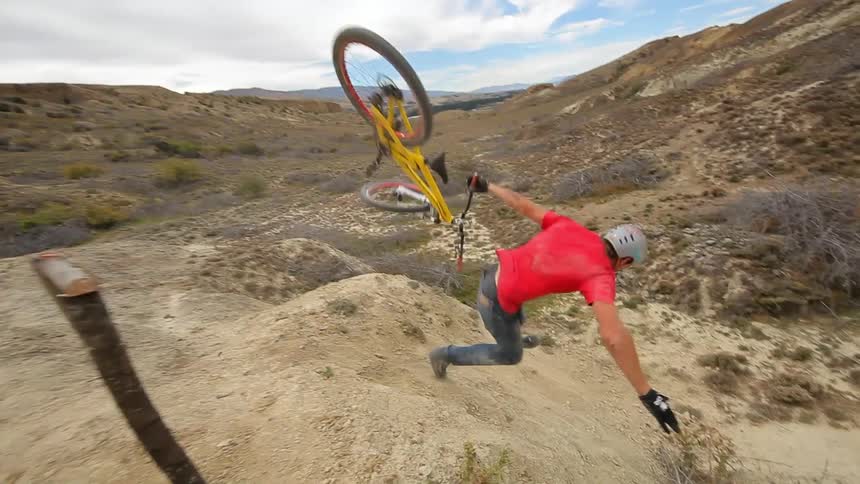 A bicyclist jumps over a dirt hill and falls off the bicycle