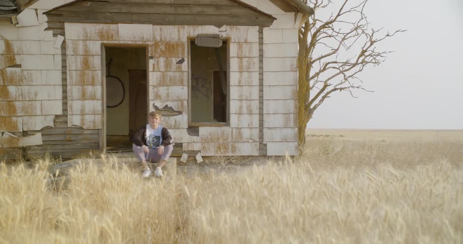 Man sits outside of an old abandoned house