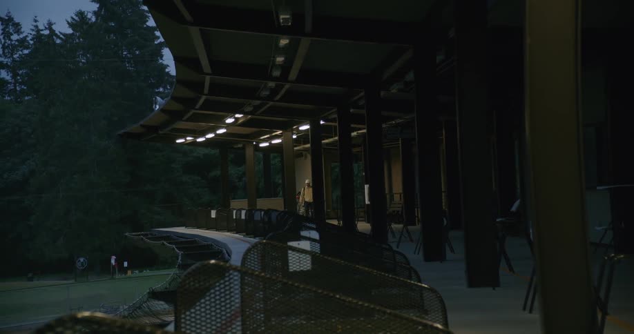 A man turns on the light and walks out onto the second level of a driving range