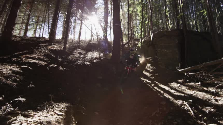 A person rides a dirt bike off a rock ledge to the path below