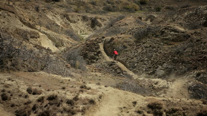 Man rides down a trail on a rocky area doing jumps