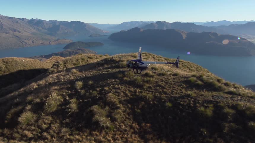 A helicopter sitting on top of a hill overlooking mountains and a lake