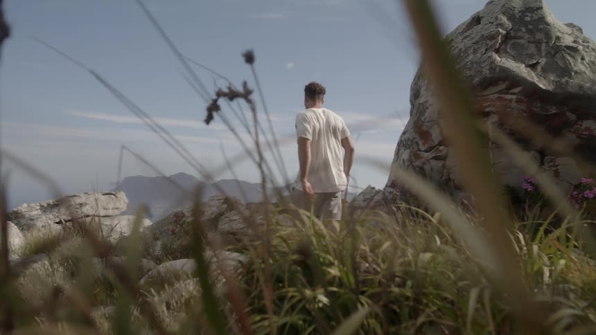 A man walks downhill past a large rock