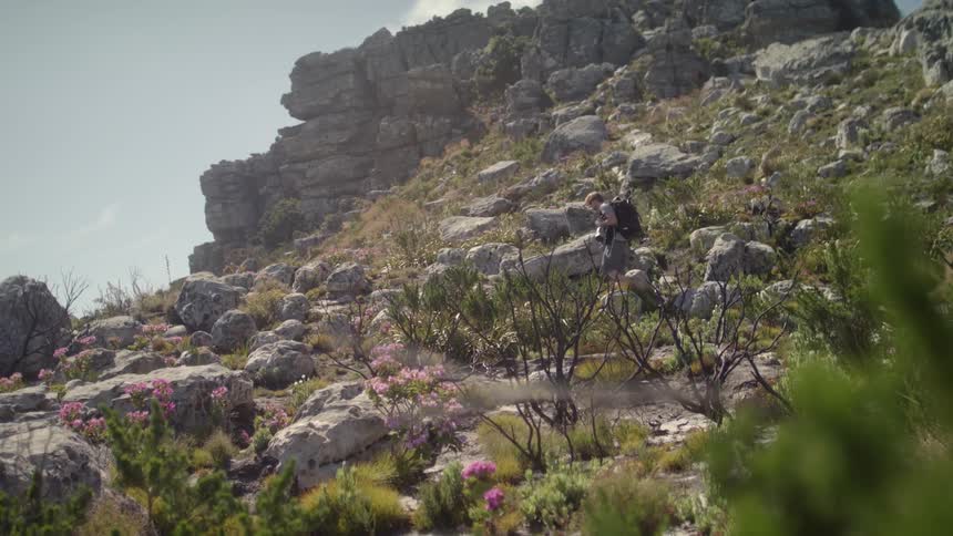 Man walks through the rocks on a hill with a backpack on his back