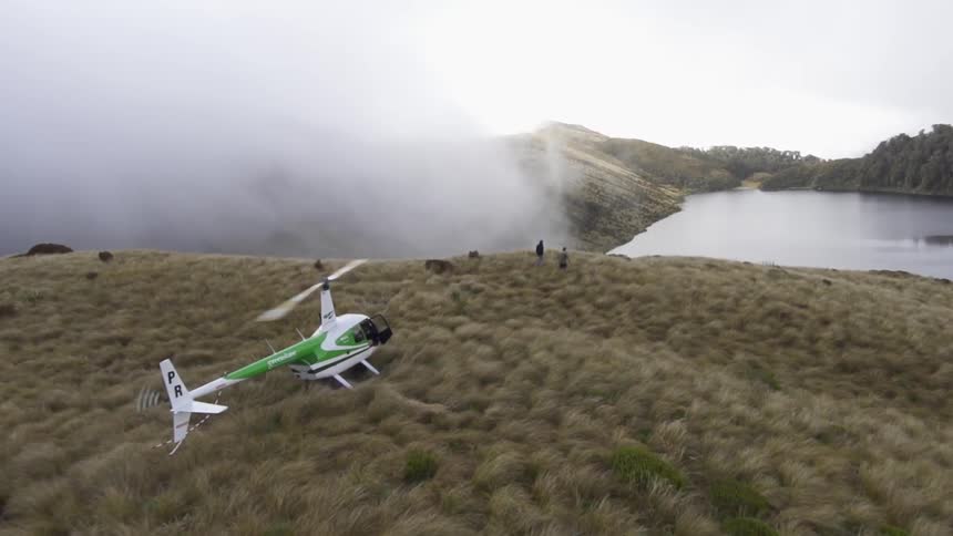 A helicopter sits on top of a hill as people walk to the edge