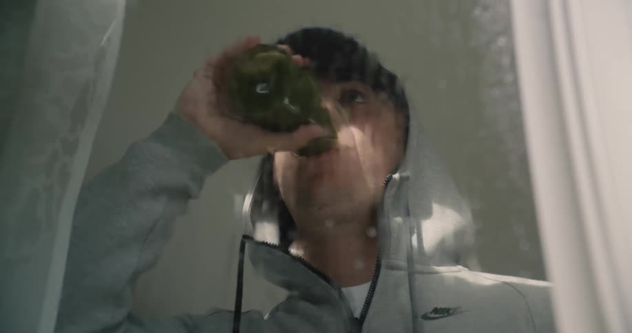 Man standing in front of a rain spattered window drinking a beverage