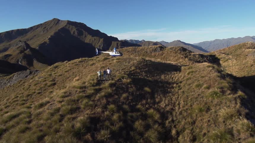 A helicopter perched on top of a mountain while three people stand and look over the area