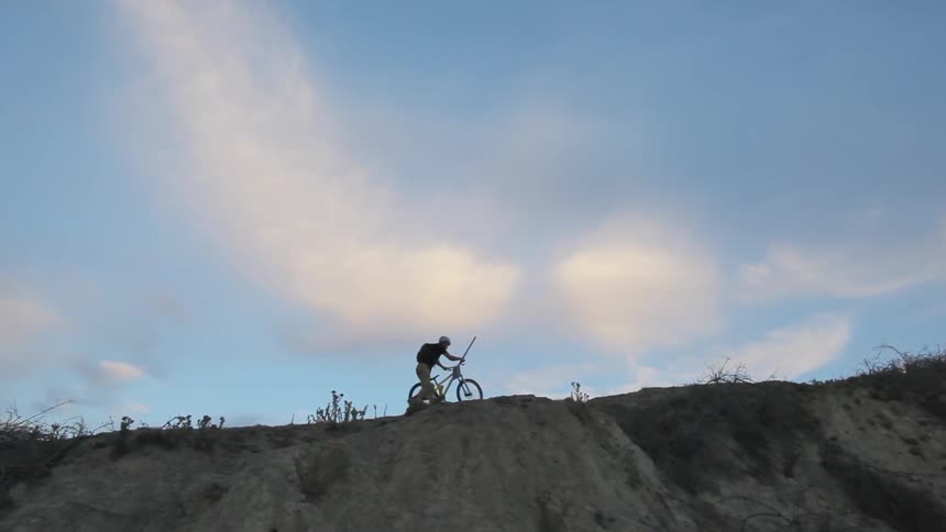 A man pushing a bicycle along the top of a cliff