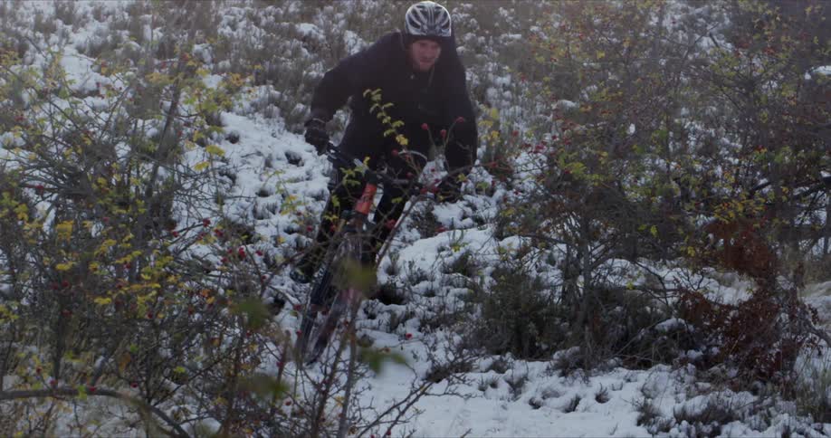 A young man riding a bike in an area covered in snow and brush