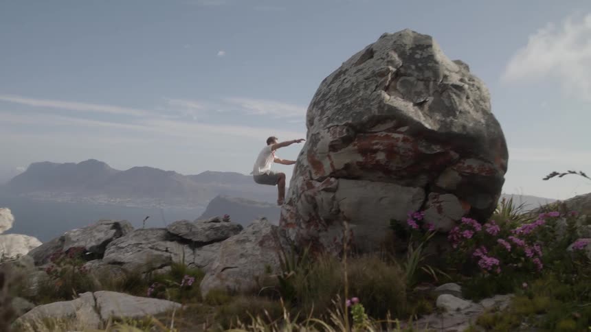 A man leaps and climbs up a rock on a sunny day
