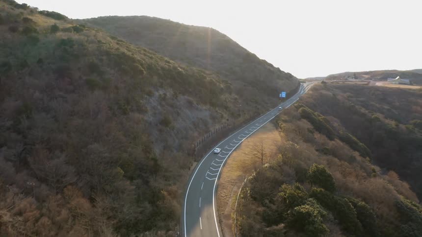 Car drives on a road winding through grassy mountain