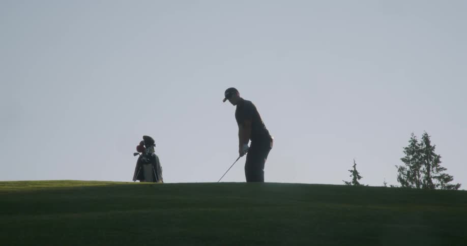 A golfer is adjusting his gloves as he approaches his ball and then takes a shot