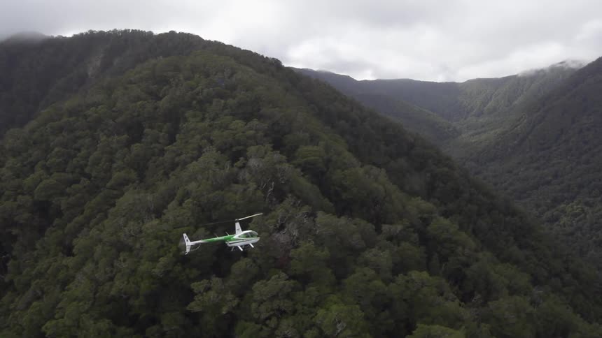 Helicopter flying over tree covered mountains