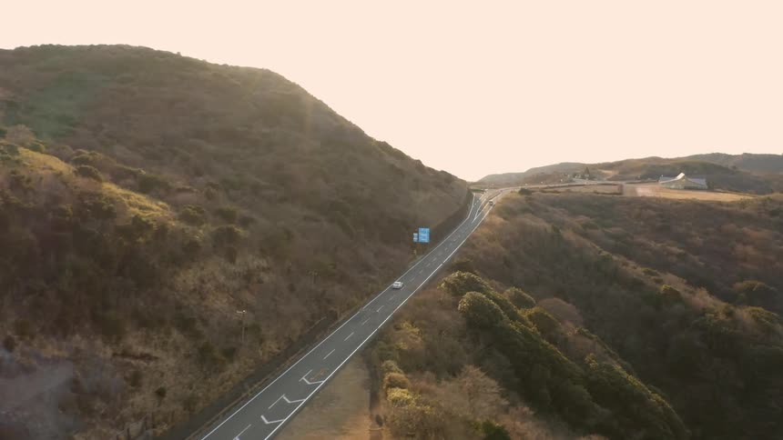 Vehicles drive on a country road through the hills on a sunny day