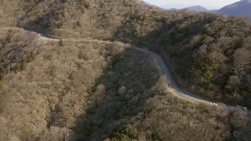 A car is driving on a road in daylight through a hilly landscape