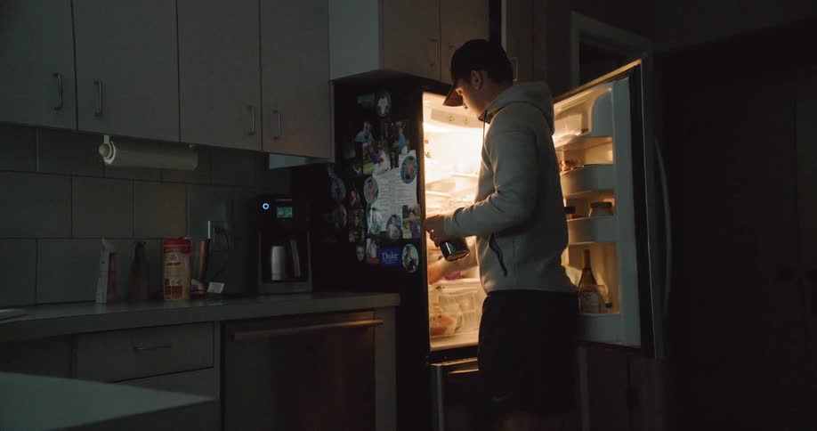 Man opens the door of a fridge in a kitchen at night