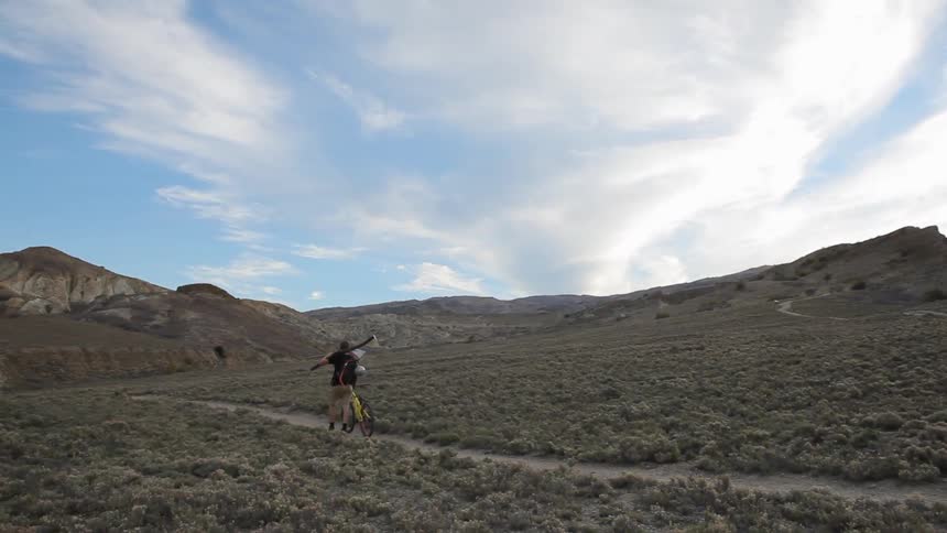 A man walking his bike as he balances a long branch on his shoulders