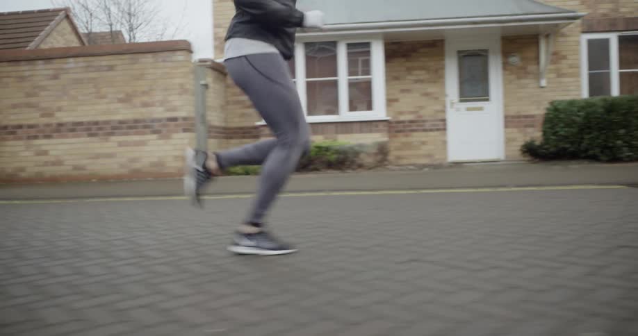 A woman is jogging on a cobblestone street through a neighborhood in daylight