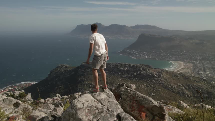 Person jumps onto a large rock on a mountain overlooking water