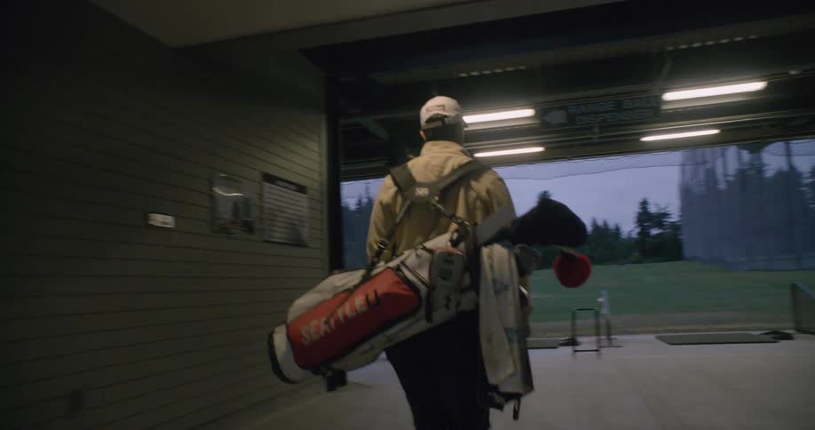 Man carrying a bag of golf clubs walks out of a building