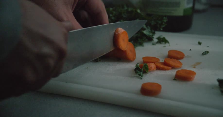 Person is chopping carrots with knife on cutting board