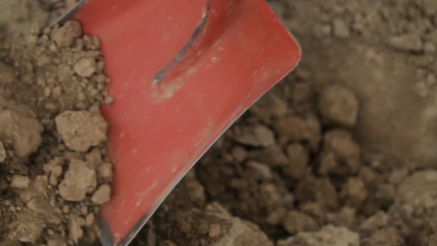 A shovel picking up hard packed clay dirt