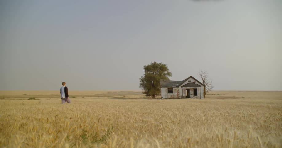 Man walking in a grassy field toward an abandoned house