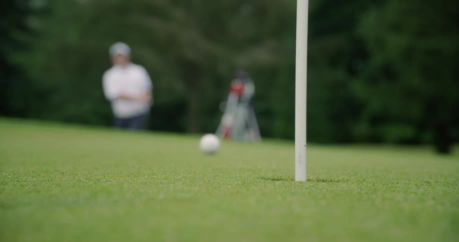 Man swings golf club and ball rolls into the hole